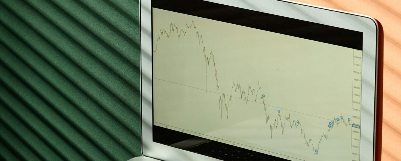 A laptop displaying financial graphs with documents on a sunlit office desk, ideal for finance themes.