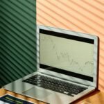 A laptop displaying financial graphs with documents on a sunlit office desk, ideal for finance themes.