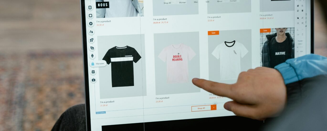 A person points to t-shirt options in an online store on a laptop screen.