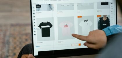 A person points to t-shirt options in an online store on a laptop screen.