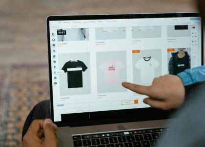 A person points to t-shirt options in an online store on a laptop screen.